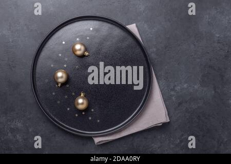 Christmas table setting. Black ceramic plate with golden balls on stone background. Gold decoration - Image Stock Photo