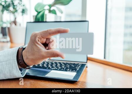 mans hand holds a card on the background of a laptop for online purchases, loan processing, discount card. mockup Stock Photo