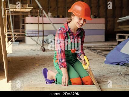 little girl working with wood. kid sawing a plank in carpentry. working with wood in a garage. happy childhood. hardworking child sawing with hand wood saw. teenage girl with hand-saw. Stock Photo