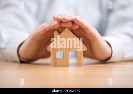 Wooden toy house protected by hands. Home insurance concept Stock Photo