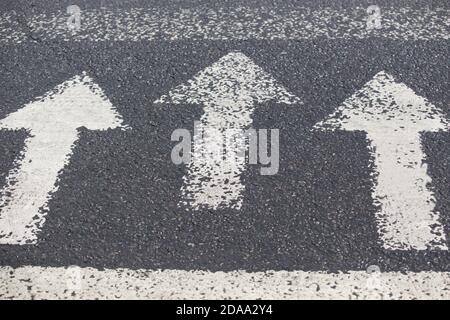 Three white arrows pointing in one direction on gray asphalt floor. Walking direction, crossroads, intersection, crossway Stock Photo