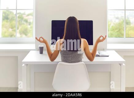 Rear view of a relaxed young woman resting and meditating during a break at work sitting at a table. Stock Photo