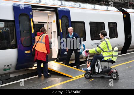 Train and station staff at Preston railway station help a disabled wheelchair user to board a train using a wheelchair ramp to access carriage. Stock Photo