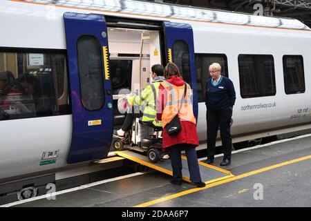 Train and station staff at Preston railway station help a disabled wheelchair user to board a train using a wheelchair ramp to access carriage. Stock Photo