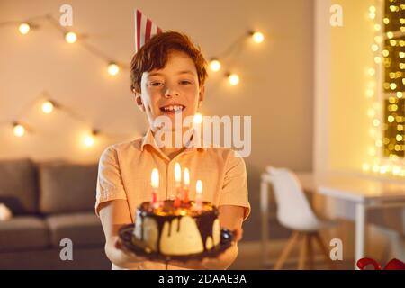 Happy little boy holding birthday cake with lit candles, looking at camera and smiling Stock Photo