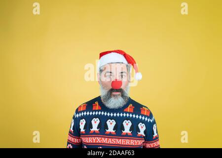 Portrait of a man in Santa Claus hat with red clown nose on yellow background Stock Photo