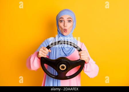 Portrait of pretty funny funky amazed muslimah lady wearing hijab holding in hand turing rudder isolated on vivid yellow color background Stock Photo