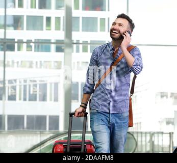 Portrait of happy male traveler walking with bag and talking on cellphone Stock Photo