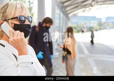 Passer-by or commuter with a face mask because of Covid-19 uses her mobile phone Stock Photo