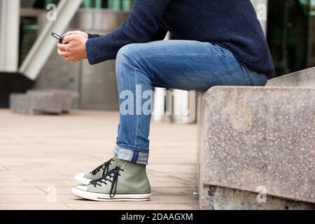 Low angle portrait of man sitting outdoors by the street and using cellphone Stock Photo
