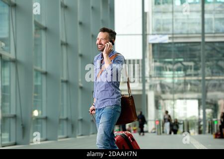 Portrait of happy mature guy walking in the train station with a mobile phone and suitcase Stock Photo