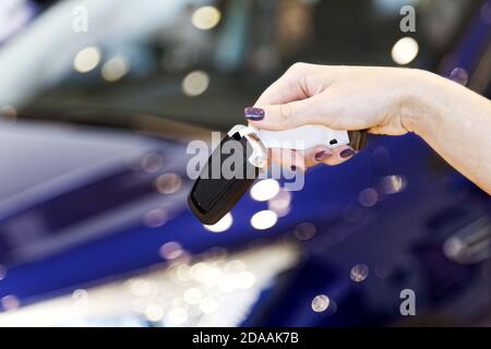 Womans hand holding car key against car on blurred background Stock Photo