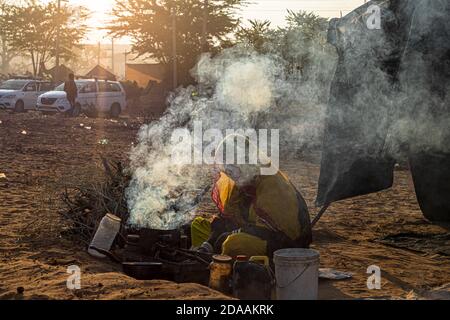 an indian woman making food, smoke is coming out from the clay handmade stove in background. Stock Photo