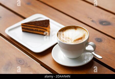 White cup of coffee cappuccino and piece of striped cake on a wooden table. Shallow focus. Stock Photo