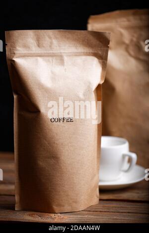 Brown craft paper bags with coffee beans on wooden table against black background Stock Photo