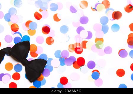 Festive, multicolored paper confetti in the form of circles and a black bow tie isolated on white background Stock Photo