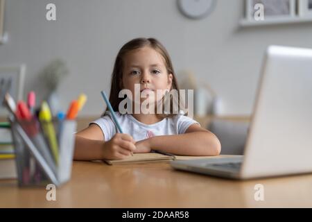 Portrait of happy small pupil learning at home. Smart kid schoolgirl looking at camera, studying remotely online Stock Photo