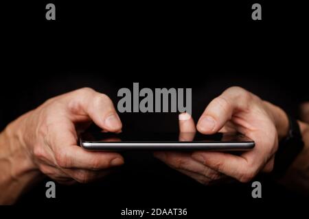 Closeup mans hand using smartphone on black background. Shallow focus. Stock Photo