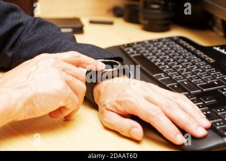 Hands of man using his smartwatch at a table next to the computers keyboard. Shallow focus. Stock Photo