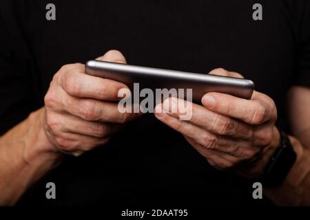 Closeup mans hand using smartphone on black background. Shallow focus. Stock Photo