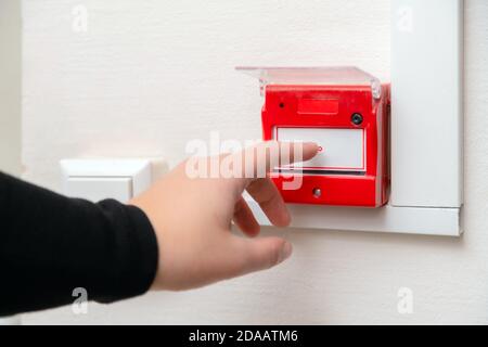 Hand pressing fire alarm button at school or business office. Close up of protection console against flame damage Stock Photo