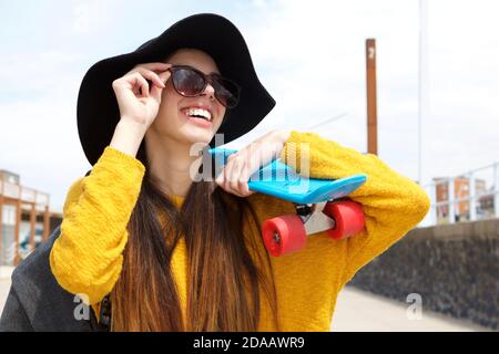 Close up portrait of smiling young woman holding skateboard on shoulder Stock Photo