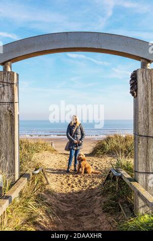 Dog walk on beach, walking dog on beach, Mablethorpe, Lincolnshire, UK, woman with dog, cockapoo, red cockapoo, posing with dog, dog walk, dog, beach, Stock Photo