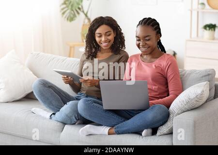 Two african female friends spending time at home, using gadgets Stock Photo