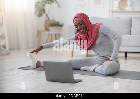 Black muslim woman in hijab exercising in front of laptop at home Stock Photo