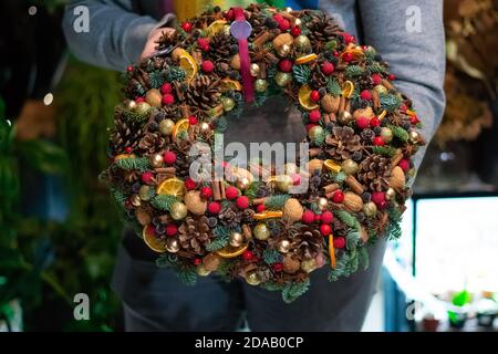 Person holding beautiful and colourful hand made Christmas wreath, green spruce branches decorated with pine cones and other decorations. Christmas ch Stock Photo
