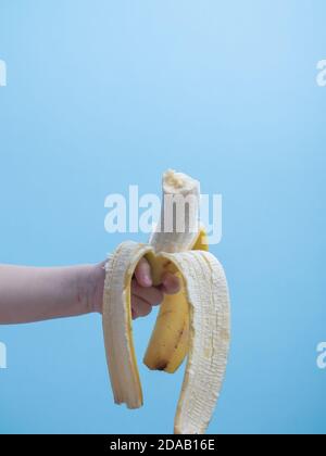a childs hand holds a bitten banana on a blue background Stock Photo