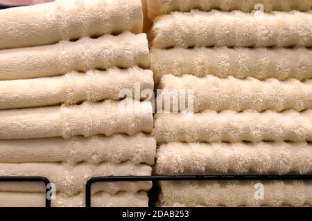 A stack of terry towels lies on a shelf in the bathroom, spa, wardrobe, laundry, shop. Hygiene items, soft bath towels in the supermarket in beige Stock Photo