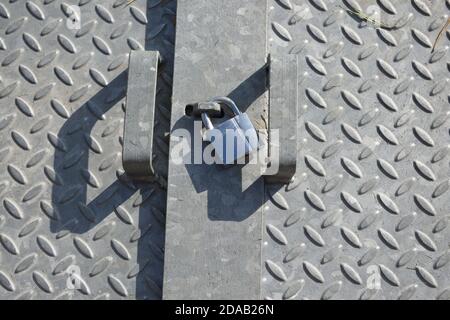 Checkered diamond patterned galvanized steel plates, lit by natural sunlight in an outdoor setting. Shiny metal padlock sits between the two handles Stock Photo