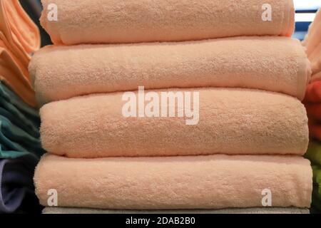 A stack of terry towels lies on a shelf in the bathroom, wardrobe, laundry, shop. Hygiene items, soft bath towels in the supermarket, beige or peach Stock Photo