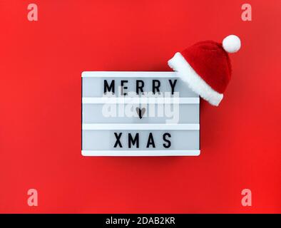 Merry xmas greeting on light box with Santa hat on a red background. Stock Photo