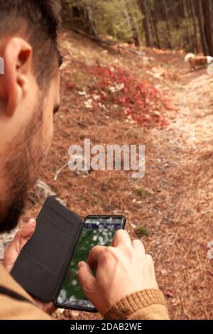 Young man using his smartphone in forest of mountain. Male hands scrolling the map in the phone close-up. Stock Photo