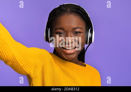 Cheerful black woman taking selfie while listening music with wireless headphones Stock Photo