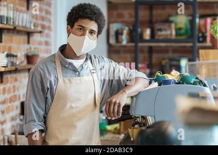 Young african american guy in apron and protective mask in modern loft coffee shop Stock Photo