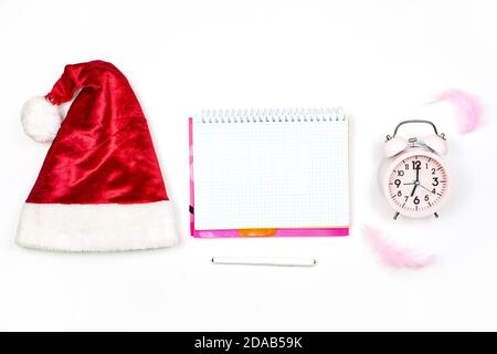 Santa cap, empty notepad and alarm clock on white. New year resolutions. Notepad with Christmas decorations. New year with new plans Stock Photo
