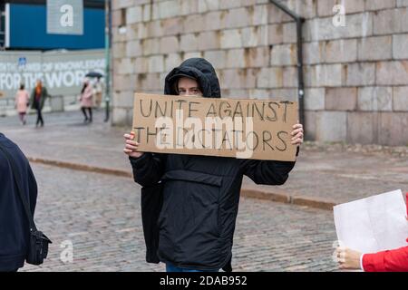 Demonstrator holding a cardboard sign saying: "Unite Against the Dictators" at Senate Square in Helsinki, Finland Stock Photo