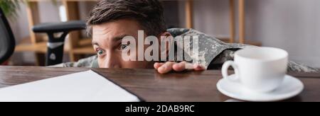 scared military man hiding under desk, banner Stock Photo