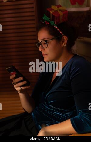 Young woman with christmas hair decor looking thoughtful into her cellphone at christmas. Stock Photo