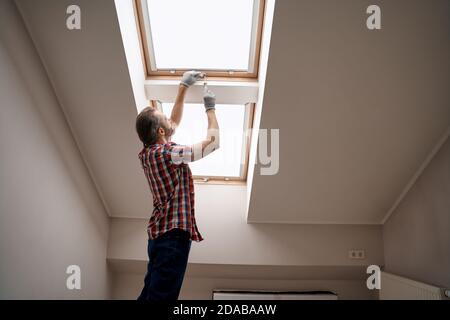 Young caucasian repairman screwing handle on skylight window Stock Photo