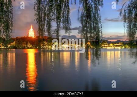 Sunset after rain on West Lake in Hangzhou, China with Leifeng Pagoda like a glowing lighthouse seen through blurry willows. Stock Photo