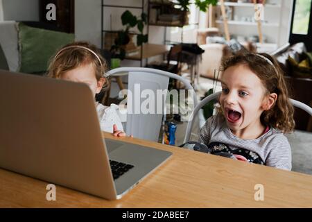 Two children watching educational movie on laptop while sitting at table in kitchen. Stock Photo