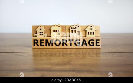 Models of a wooden house. Word 'remortgage' on wooden block. Copy space. Business concept. Beautiful wooden table, white background. Stock Photo