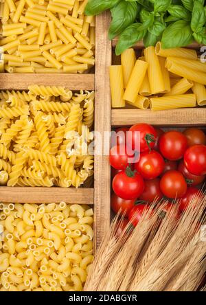 Wooden box with various classic italian pasta and basil with cherry tomatoes. Top view Stock Photo