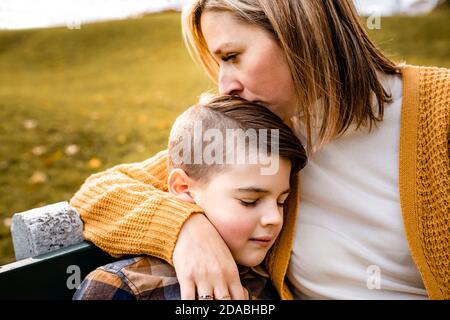 mother consoling child boy in the autumn leaf fall sit on bench Stock Photo