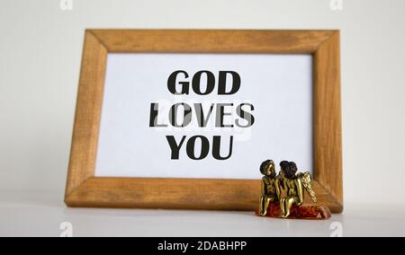 Wooden picture frame with inscription from Bible on beautiful white fon. Two bronze angeles on the table. Stock Photo