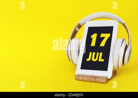 July 17th. Day 17 of month, Calendar date. Stylish headphones and modern tablet on yellow background. Space for text. Education, technology, lifestyle Stock Photo